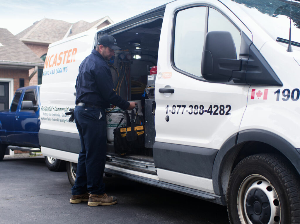 An HVAC service technician unloads his tools from a parked Lancaster Heating and Cooling van 