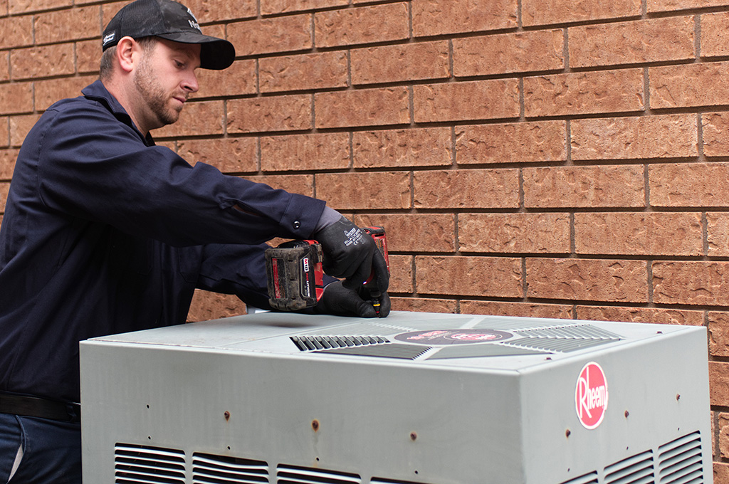 A Lancaster Heating and Cooling service technician repairs a Rheem air conditioner.